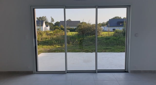 Vue sur un jardin depuis l'intérieur d'une maison, à travers une baie vitrée